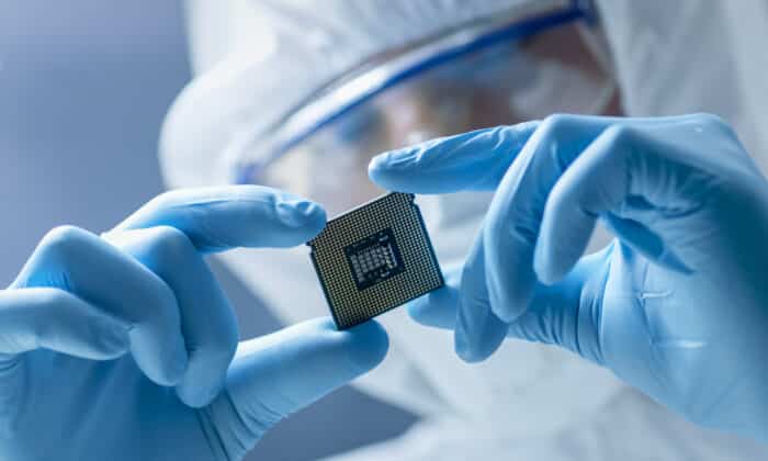 In Ultra Modern Electronic Manufacturing Factory Design Engineer in Sterile Coverall Holds Microchip with Gloves and Examines it.